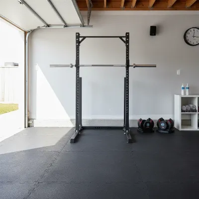 A well-organized budget garage home gym with essential equipment like a squat stand, adjustable dumbbells, and horse stall mats on the floor.